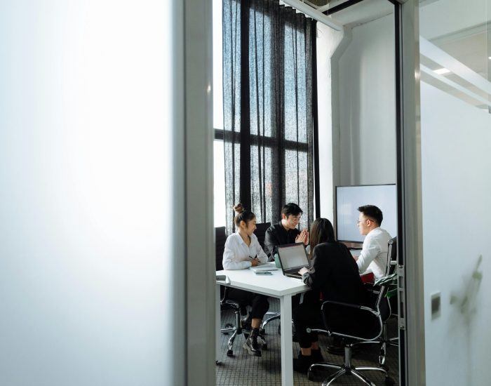 Group collaborating in a well-lit office room with large windows, discussing business strategies.